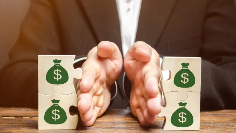 Mãos separando peças de quebra-cabeça com símbolos de dinheiro, representando divisão de bens.