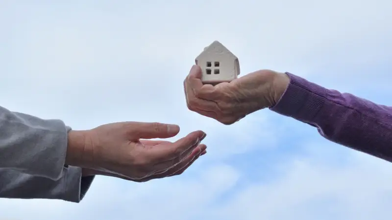 Posso doar alguns dos meus bens para somente um dos meus filhos? 1 Mão entregando uma pequena casa de modelo para outra pessoa, simbolizando doação ou transferência de propriedade.